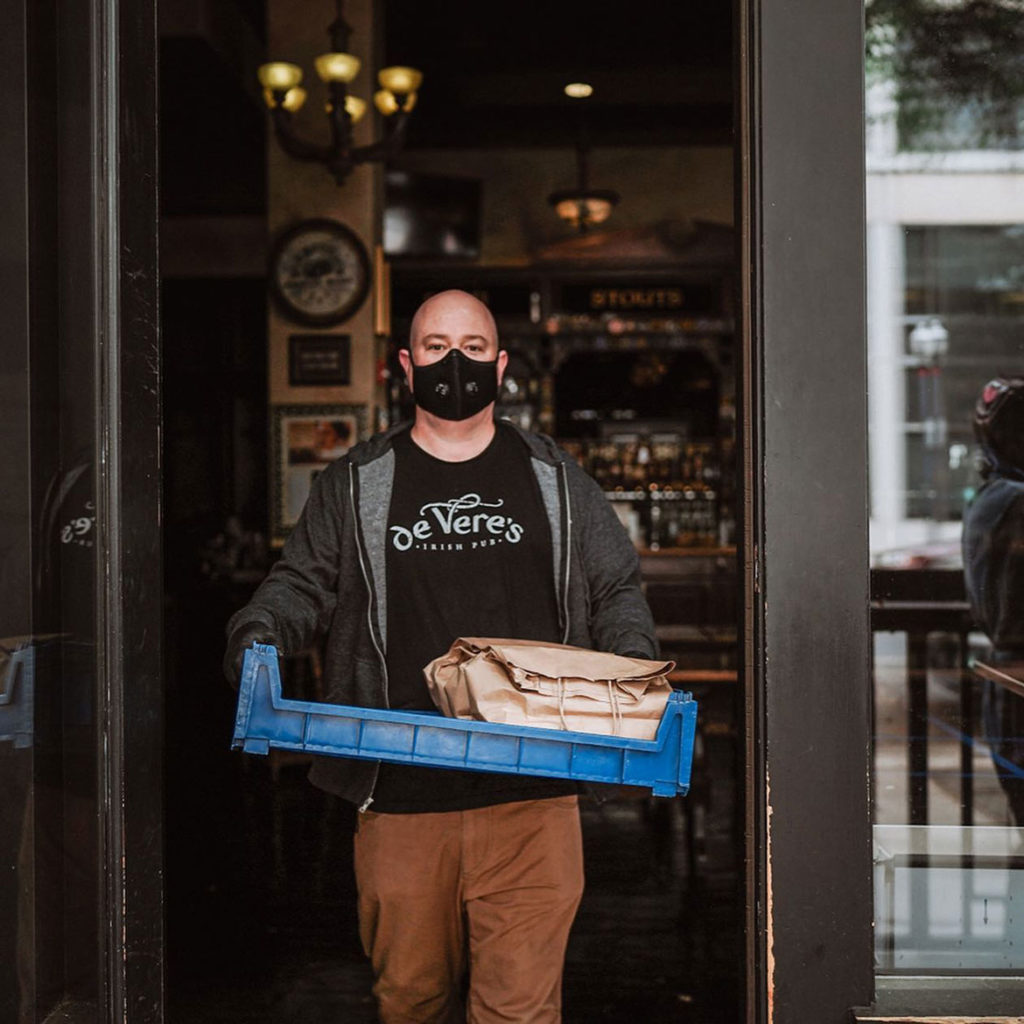 A restaurant worker in gloves and a mask is carrying a to-go order in a tray to prevent the spread of Covid-19.