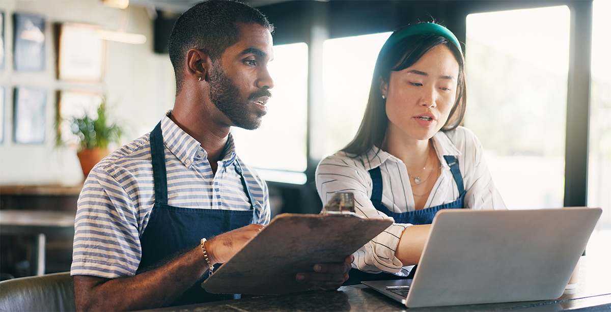 Two business owners in the restaurant industry reviewing their budget and business plans while sitting on a brightly lit empty restaurant room